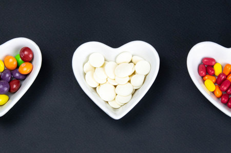 Heart shaped saucer filled with colorful candies on a black background. Valentine's Day illustration. Top viewsの写真素材