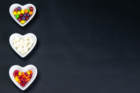 Heart shaped saucer filled with colorful candies on a black background. Valentine's Day illustration. Top views with clear spaceの写真素材
