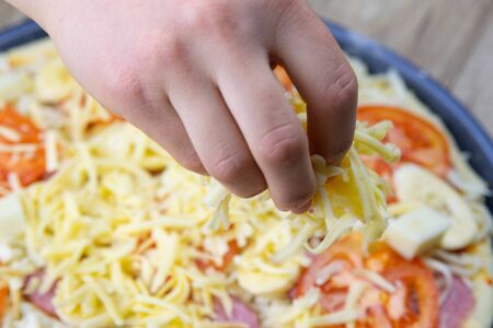 The woman's hand sprinkles pizza preparation with mozzarella cheese, tomatoes, salami and bananas on the very preparation of decompositionの写真素材