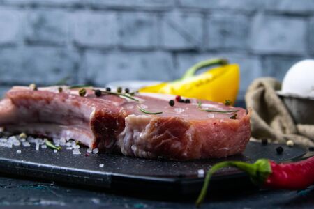 Raw pork steak on the bone near rosemary, corn, eggs and bell pepper. Marbled farm meat. Gray background. Top viewの写真素材