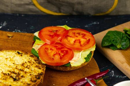Process of cooking burgers. Cropeed view of chef hands in black gloves with prepared cheeseburger, variety of fillings and ingridients on wooden desk. Catering and Good Quality Fastfood conceptの写真素材