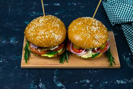 Two homemade beef burgers with mushrooms, micro greens, red onion, fried eggs and beet sauce on wooden cutting boardの写真素材