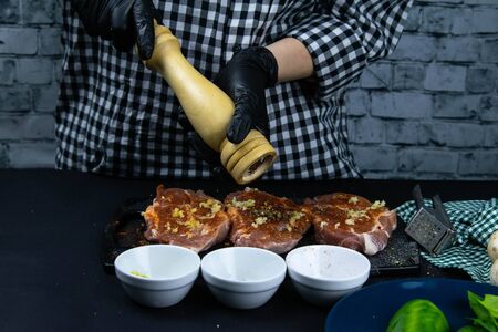 A chef in black gloves sprinkled with pepper from hand pepper a raw tenderloin. Fresh raw pork tenderloin on a wooden cutting board. Close up.の写真素材