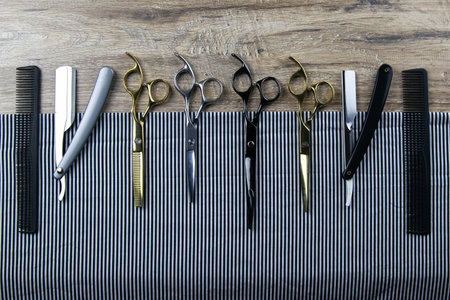 A set of scissors for haircuts, combs and a dangerous razor spread on a striped towel that stands on...