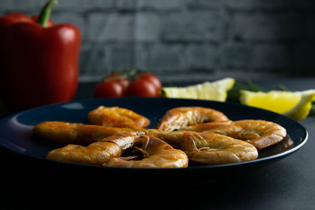 Closeup of cooked shrimps served on blue plate with paper, tomato, lemon and herbs