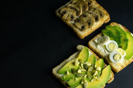 Three sandwiches on a wooden board, a mushroom sandwich, an avocado and seeds sandwich and a sandwich with avocado and eggs. Top views with clear spaceの写真素材