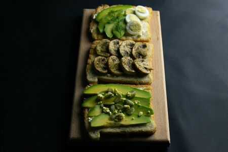 Three sandwiches on a wooden board, a mushroom sandwich, an avocado and seeds sandwich and a sandwich with avocado and eggs. Top viewsの写真素材