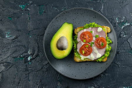 Sandwich with ham and tomatoes on gray plate with avocado. Top views with clear space