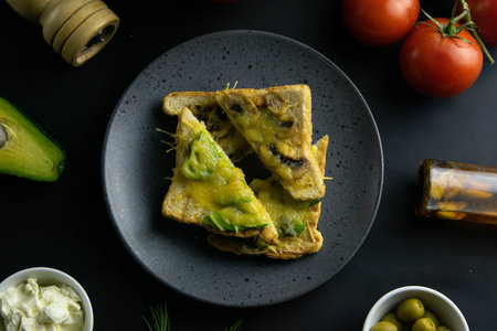 Delicious sandwiches with avocado, mushrooms and cheese cut into pieces on grey plate close-up. Next...
