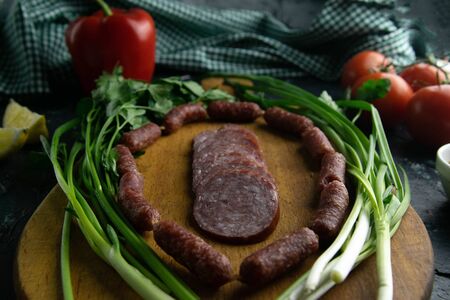 Sliced salami on a wooden board, around the ham, green onions, dill and parsley. Top viewsの写真素材