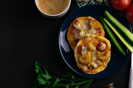 Small mini pizza with mushrooms and cheese, and pizza with ham and cheese on blue plate with...