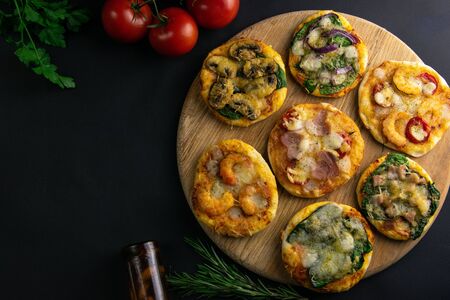 Small mini pizza. Set of different mini pizzas. Pizza on wooden board : with shrimp, with mushrooms, with spinach and onions, with bacon, with paperoni, with tomatoes. Top views with clear spaceの写真素材