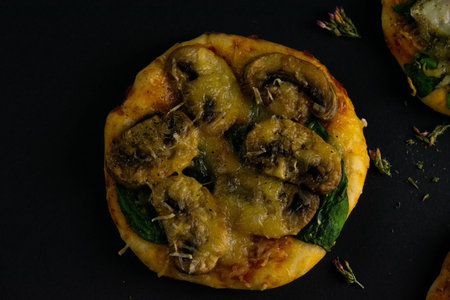 Small mini pizza. Pizza with mushrooms, spinach and cheese on black background. Pieces of other...