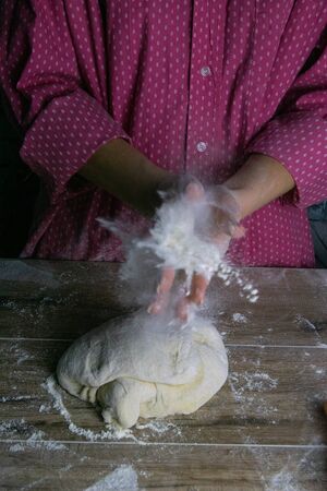 A woman claps her hands around the go splashes of flour. Process of preparation of dough for baking bread. Front viewsの写真素材