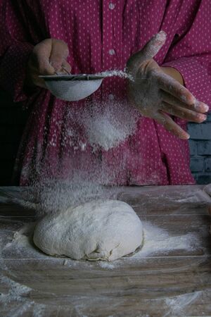 The woman sprinkles flour dough from the fullness for sifting flour, flour falls on the dough, a beautiful scattering of flour. Prepare to make bread and pastries. Front viewsの写真素材