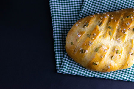 Bread on a checkered towel, a white green towel stands against a dark background. Top views with...