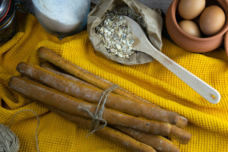 Concept shot of spice bread sticks with a wooden spoon on the wood table, oatmeal and a skein of bag...