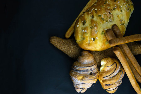 Different kinds of fresh bread with grain on black rustic background. Top views with clear space
