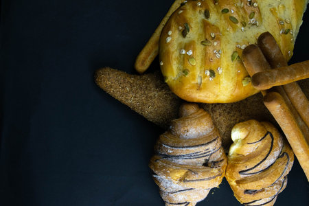 Different kinds of fresh bread with grain on black rustic background. Top views with clear space
