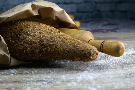 A loaf of bread together with a rocking for dough in a craft bag stand on a wooden table. Top views with clear spaceの写真素材