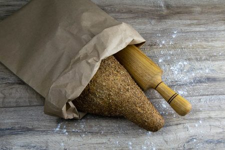 A loaf of bread together with a rocking for dough in a craft bag stand on a wooden table. Top views...
