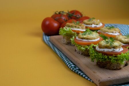 Sandwich with lettuce, cheese, tomatoes and roasted courgettes, on top is a piece of dill, all standing on a wooden board on an orange background. Top views with clear spaceの写真素材