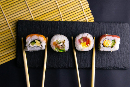 Sticks hold rolls that stand on a black graphite board for sushi that stands on a black background...