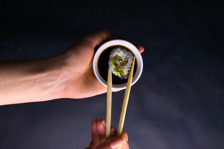 Sticks shave the roll of poppies over a plate of soy sauce, a plate in a beautiful female hand over a black background. Top viewsの写真素材