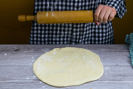 A woman sprinkles flour on a dewy pizza dough. Fresh original italian raw pizza. Preparatory...