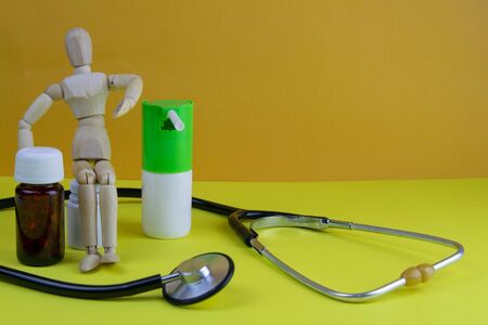 Wooden toy figure with pills on yellow background. Various capsules, tablets and medicine on blue pastel trendy background.の写真素材