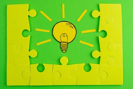 Composition with cut out paper, a picture of a light bulb located between laid out puzzles on a green background. Creative concept symbolizing the idea.の写真素材