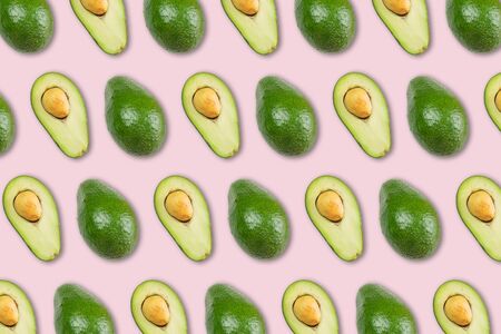 Organic avocado with seed, avocado halves and whole fruits on pink background. Top view. Creative summer food concept. Green avocadoes pattern in minimal flat lay style.の写真素材