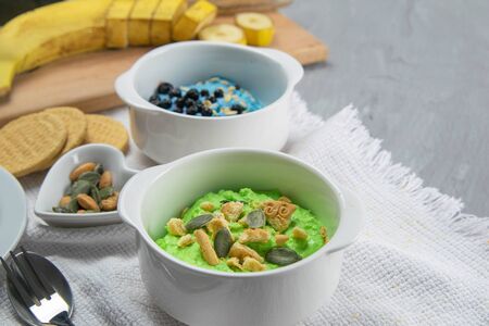 Two curd desserts: one with blueberries and nuts and the other with avocado and kiwi, next to there are pumpkin seeds and nuts.の写真素材