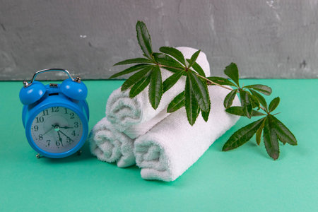 Three towels with a branch and a beautiful blue clock on a turquoise background. Concept, time to...