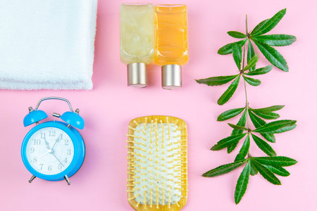 Three towels, body care oils with a branch and a beautiful blue clock on a pinc background. Concept,...