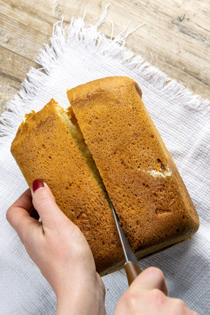 Women's hands cut fresh baked homemade bread, which stands on a white towel.
