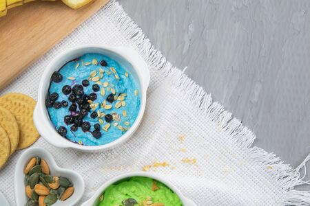 Two curd desserts: one with blueberries and nuts and the other with avocado and kiwi, next to there are pumpkin seeds and nuts.の写真素材