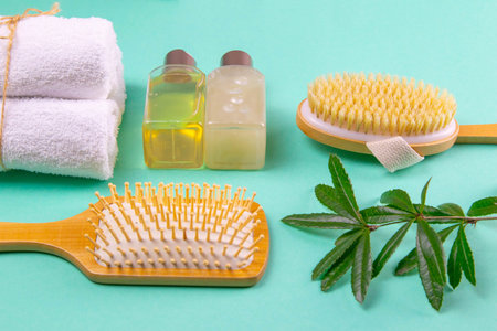 Three towels, body care oils, a green branch, sprout and a brush stand on a green background. The...