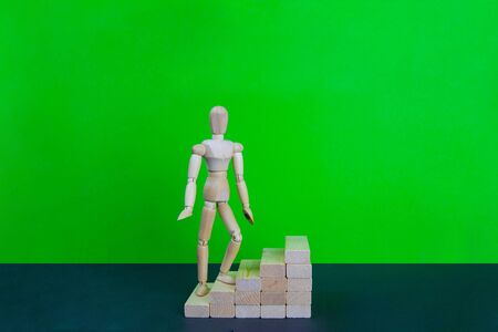 Wooden man walk up the career stairs. Ladder made with wooden bricks. Mannequin on top of development. Concept of personal development, career , changes, success. Green background, copy space for ad.の写真素材