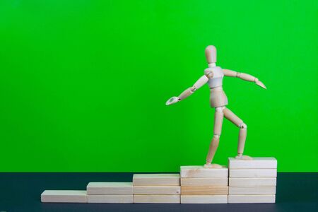 Wooden man walk up the career stairs. Ladder made with wooden bricks. Mannequin on top of development. Concept of personal development, career , changes, success. Green background, copy space for ad.の写真素材