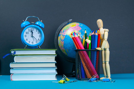 The globe and the clock stand on a stack of books, next to a glass of pencils and the pyramid is...