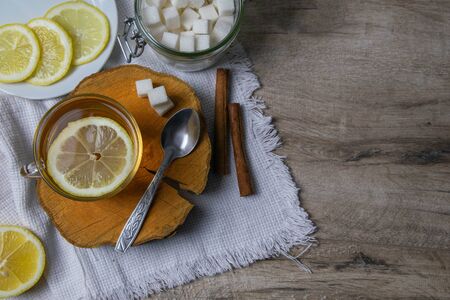 Glass transparent cup with mint tea stands on a wooden stand, next to a sugar bowl with sugar cubes, sliced lemon and a spoon.の写真素材