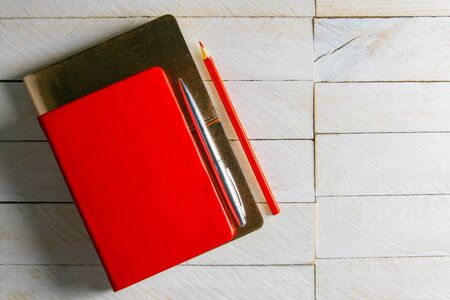 The red notebook stands on gold notebook, on the white wooden table next to stands a red pencil.の写真素材