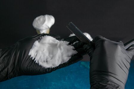 Hand holds brush for applying foam to the beard, foam and dangerous razor on blue background. Hairdressing concept.の写真素材