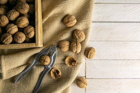 Walnuts in a wooden box, which stands on an old rustic sack, also scattered on a white table nearby...