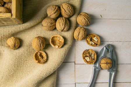 Walnuts in a wooden box, which stands on an old rustic sack, also scattered on a white table nearby...