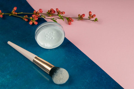 Make-up brush and powder for make-up stand on a blue-pink background.
