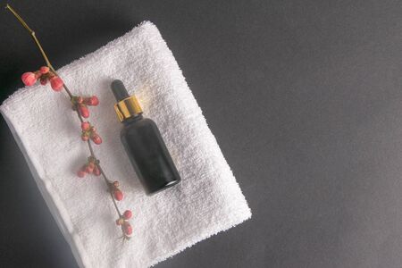 Hand oil and a branch with blooming pink flowers stand on a white towel which stands on a black background. Flat lay styling. Copy space.の写真素材
