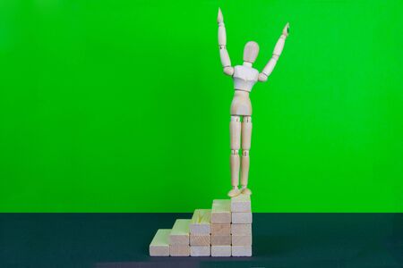 Wooden man walk up the career stairs. Ladder made with wooden bricks. Mannequin on top of development. Concept of personal development, career , changes, success. Green background, copy space for ad.の写真素材