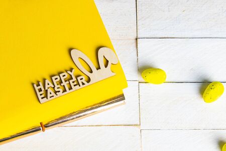 Yellow notepad with wooden rabbit, and yellow eggs on a white wooden table.の写真素材